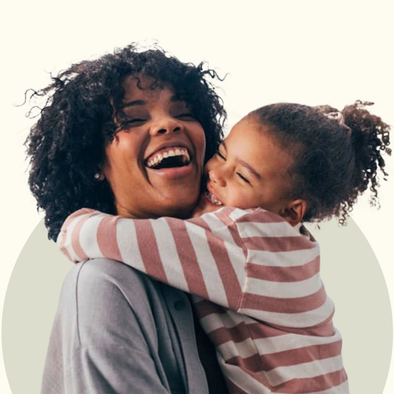 A person with curly hair is holding a child who is wearing a pink and white striped shirt.