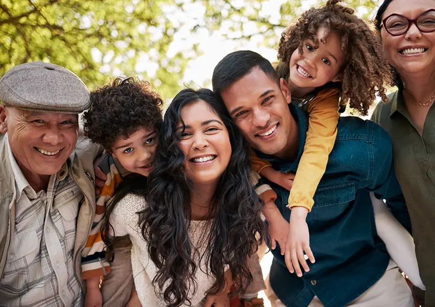 Multi-generational, diverse family smiling and embracing outdoors, symbolizing health, connection, and community.
